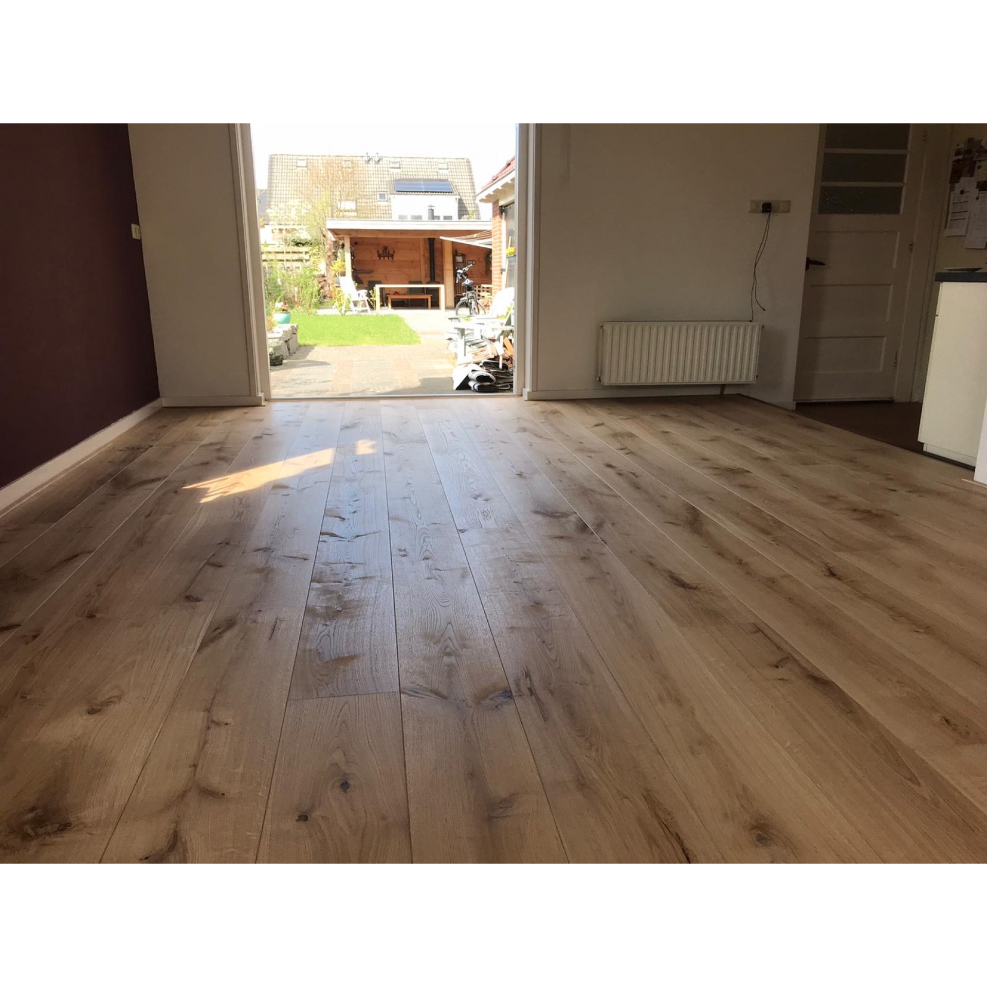 De eiken vloer sluit aan op de openslaande deuren naar de tuin. Graag een mat buiten plaatsen om het zand aan af te vegen..